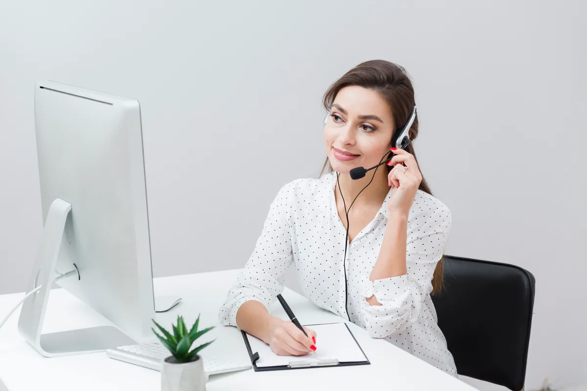 A smiling woman taking notes while talking on a headset