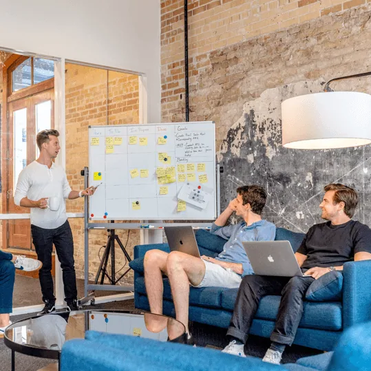 A strategist presenting ideas on a whiteboard to two colleagues working on laptops