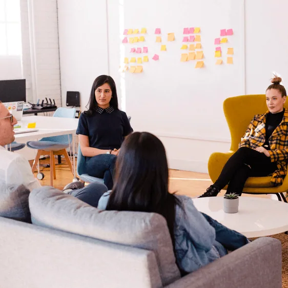 A team meeting in a lounge area in front of a wall of sticky notes
